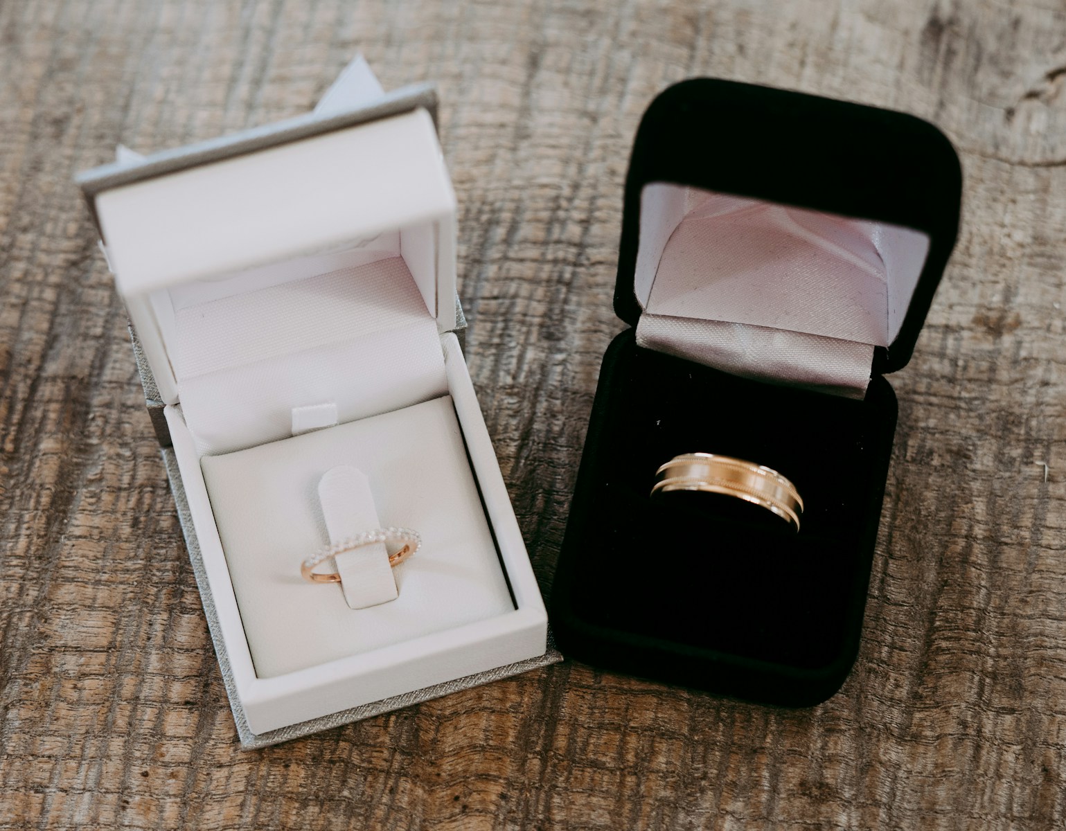 two gold-colored rings inside cases place on brown surface