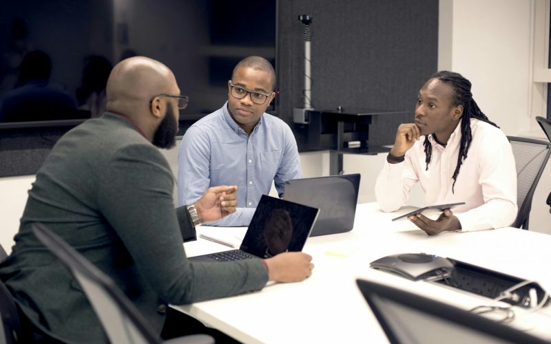 a group of people sitting around a table with laptops