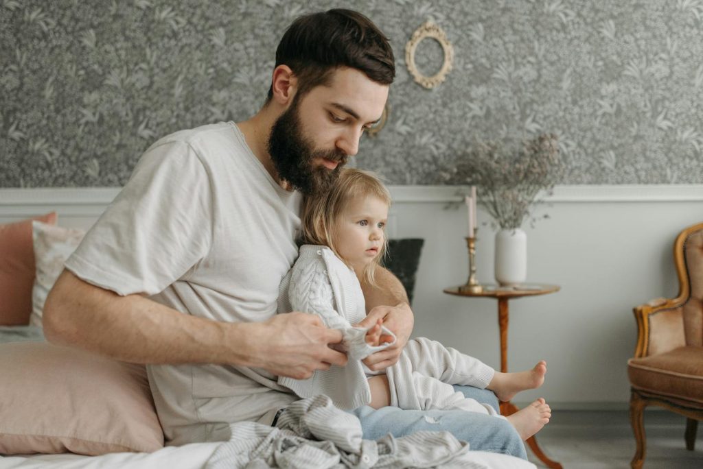 Father helping daughter get dressed in a cozy bedroom environment, highlighting nurturing parenting moments.