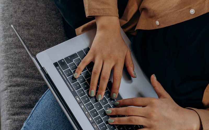 A person typing on a laptop while seated on a couch with casual attire, perfect for remote work imagery.