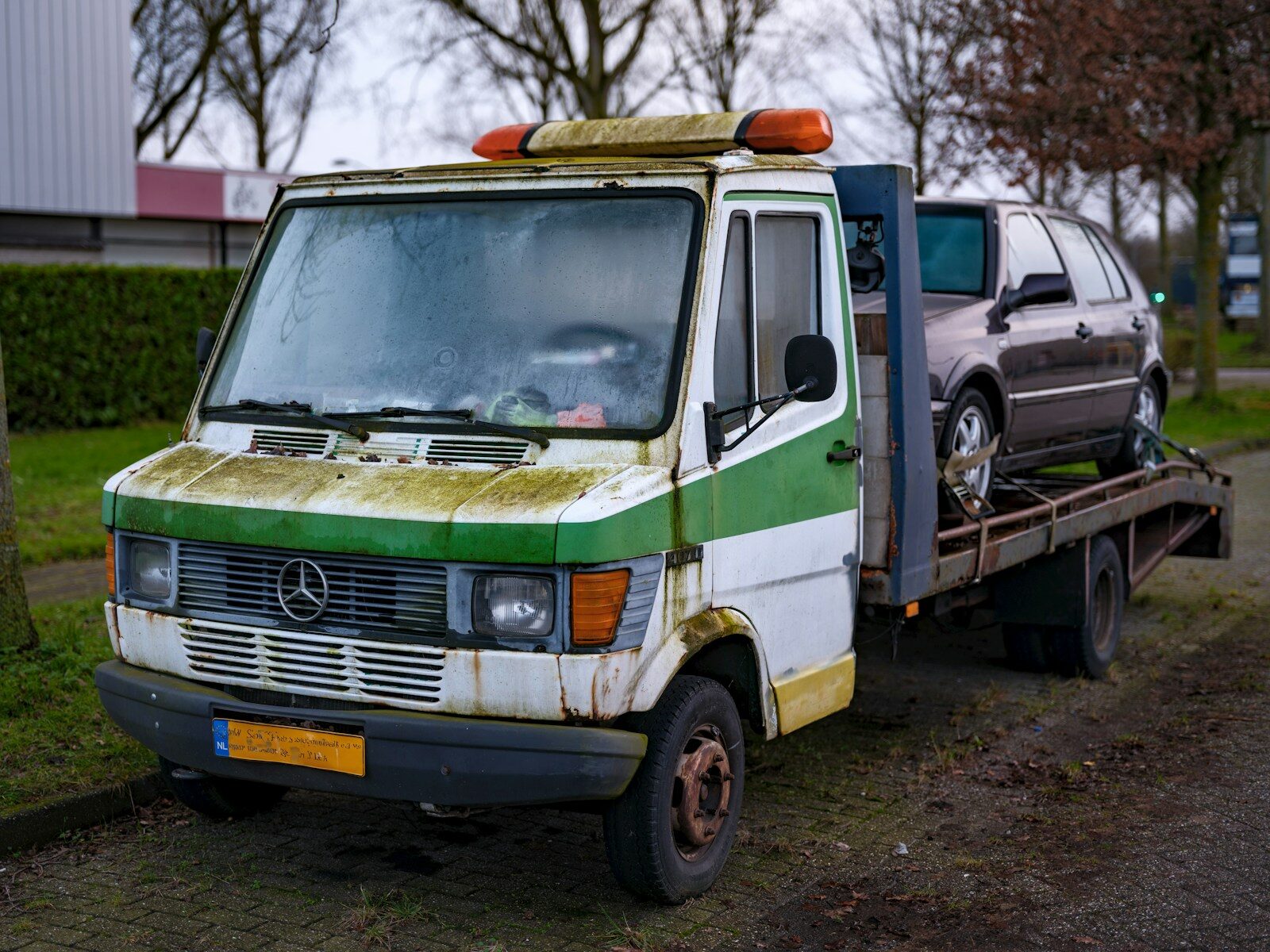 An old green and white van is being towed by a tow truck